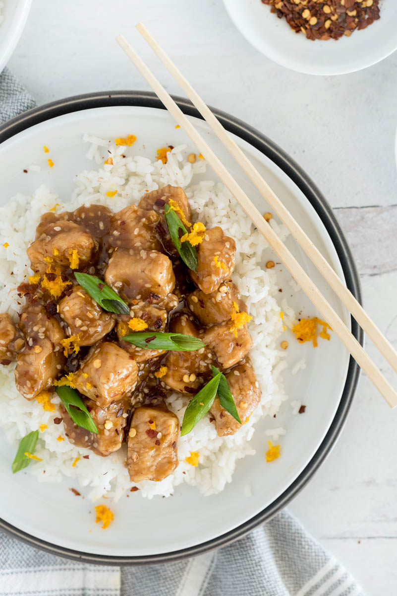 A close up of the teriyaki chicken, served over a bed of rice, with orange zest and green onions on top for garnish