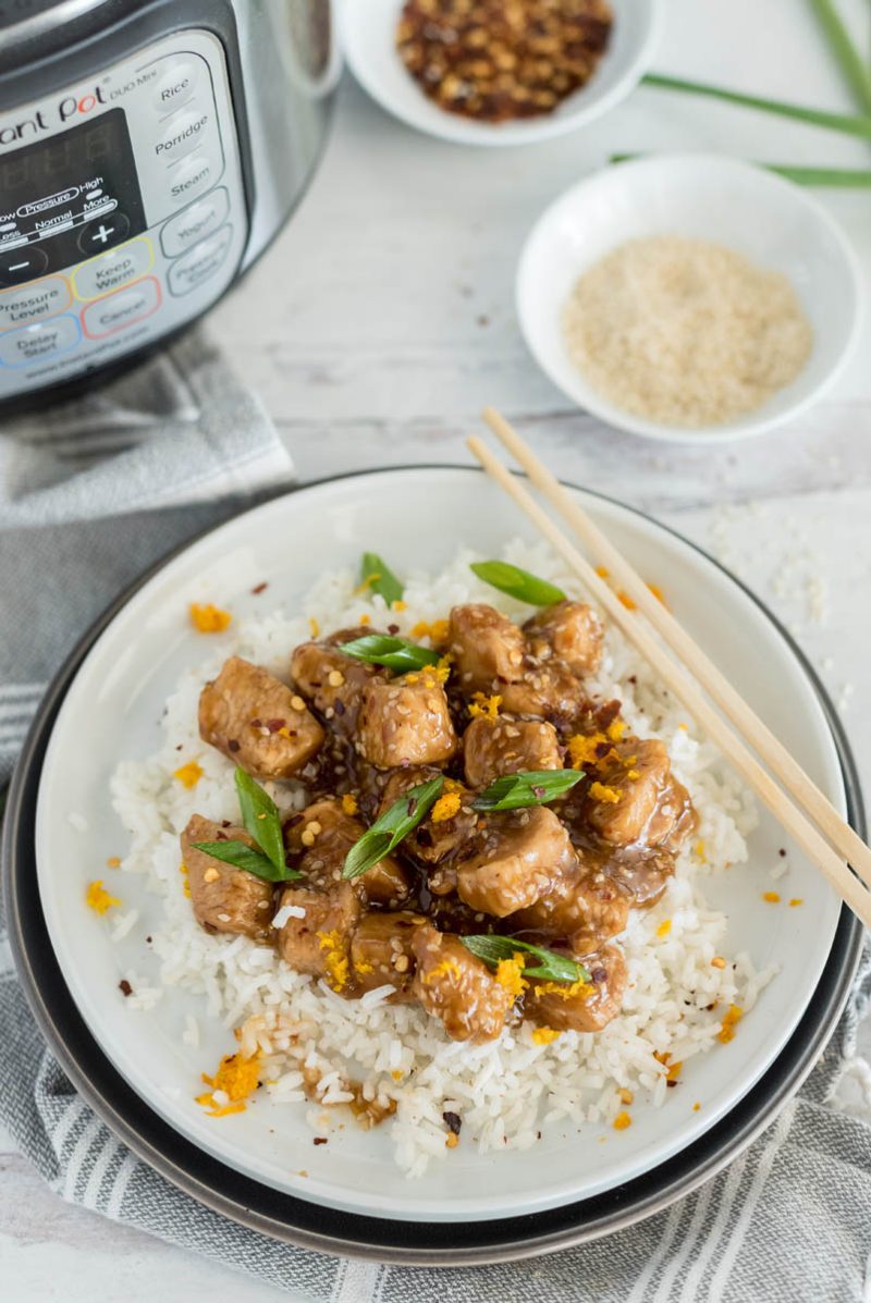 Pressure cooker Teriyaki chicken, served up on a bed of rice, garnished with green onions, with a pair of chopsticks balanced on the plate and an Instant Pot in the background left