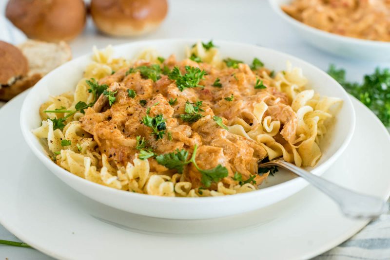 Close up picture of Instant Pot paprika chicken served over egg noodles with fresh parsley on top.