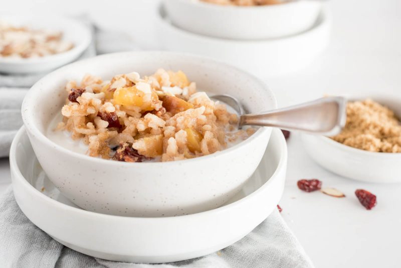 a white bowl of Instant Pot Apple Risotto with Cherries and diced apples, with a silver spoon sticking out the side and topped with additional milk