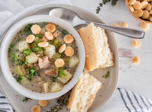 Close up, overhead shot of Instant Pot light clam chowder served in a white bowl and garnished with oyster crackers and fresh parley.