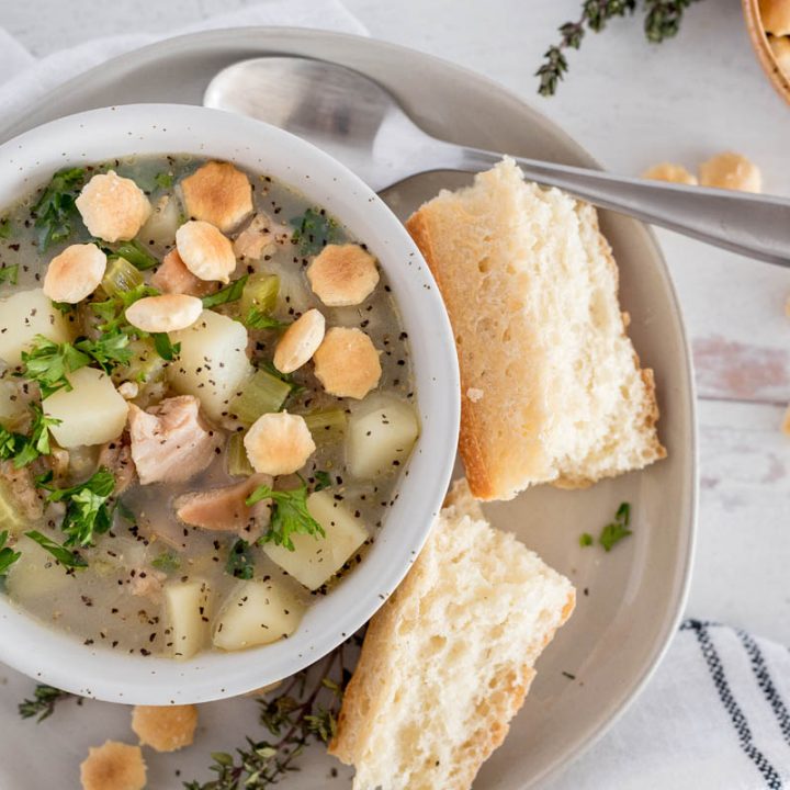 Close up, overhead shot of Instant Pot light clam chowder served in a white bowl and garnished with oyster crackers and fresh parley.