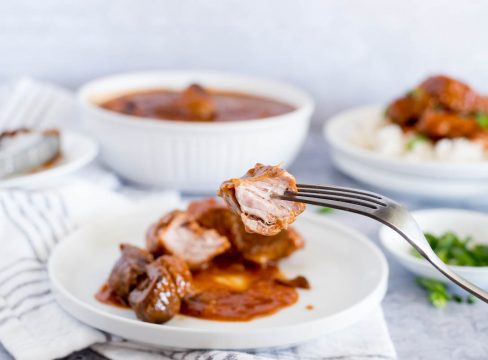 Instant Pot country style pork ribs close up of a bite of rib, with a plate full of ribs and BBQ sauce in the background