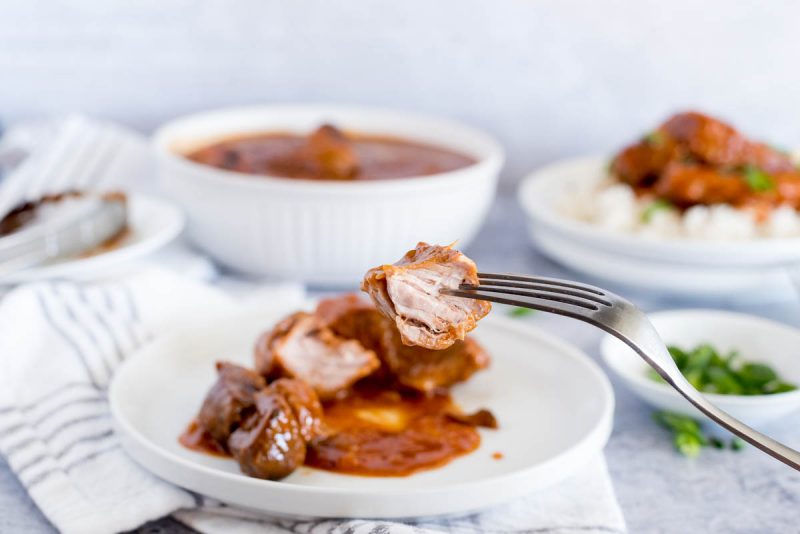 Instant Pot country style pork ribs close up of a bite of rib, with a plate full of ribs and BBQ sauce in the background