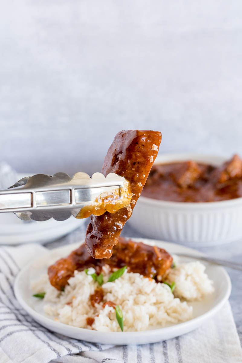 tongs holding a pork rib on a plate with rice