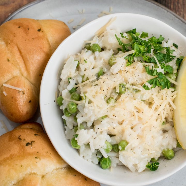 Close up overhead picture of lemon risotto made in an Instant Pot with peas, fresh parsley, parmesan, and a lemon wedge, next to some rolls.