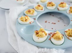45 degree overhead of a blue circular egg tray filled with Instant Pot BBQ deviled Eggs with crumbled bacon with one egg removed.