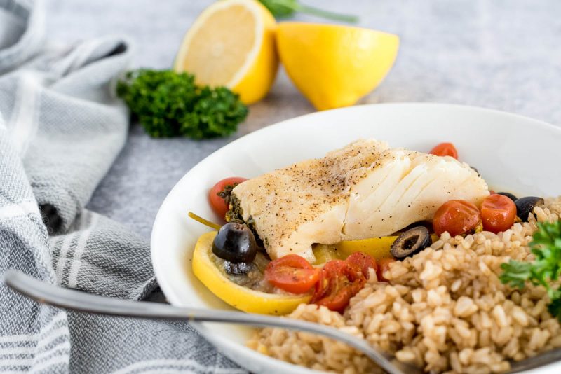 mediterranean fish on a white plate with brown rice and lemons