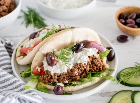 plate with two greek beef tacos topped with tzatziki sauce, olives, cucumbers and dill