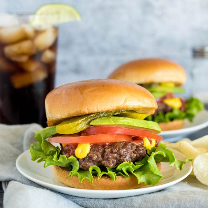 onion burgers on buns with toppings in front of a glass of soda