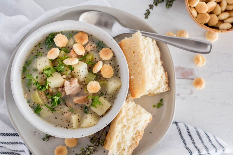 Close up, overhead shot of Instant Pot light clam chowder served in a white bowl and garnished with oyster crackers and fresh parley.