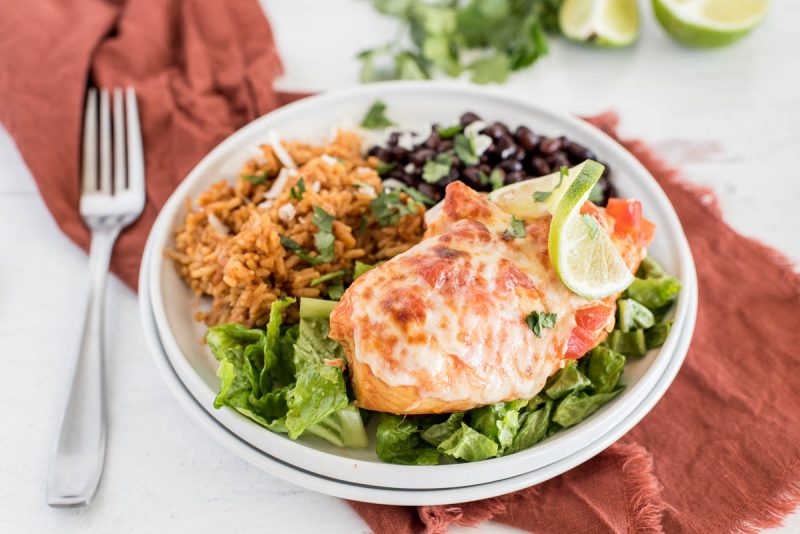 a 45 degree closeup horizontal shot of Instant Pot Salsa Chicken, plated on a white plate and served on top of a bed of shredded lettuce, with Mexican rice and black beans in the background