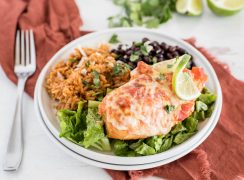 a 45 degree closeup horizontal shot of Instant Pot Salsa Chicken, plated on a white plate and served on top of a bed of shredded lettuce, with Mexican rice and black beans in the background