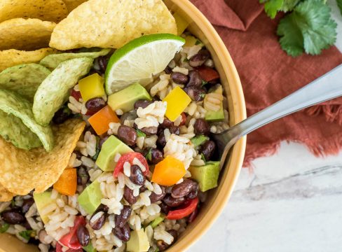 close up on a bowl of brown rice and black bean salad wth tortilla chips and lime