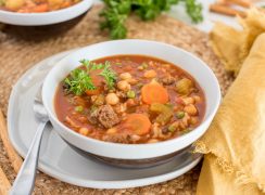 Close up picture of Instant Pot vegetable beef and rice soup served in a white bowl. Placed on a woven mat, next to a yellow linen napkin.