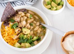 bowl of instant pot white chicken chili with avocado, chips and shredded cheese on top