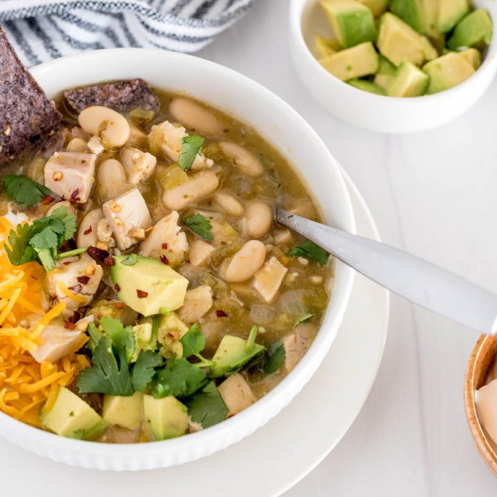 bowl of instant pot white chicken chili with avocado, chips and shredded cheese on top