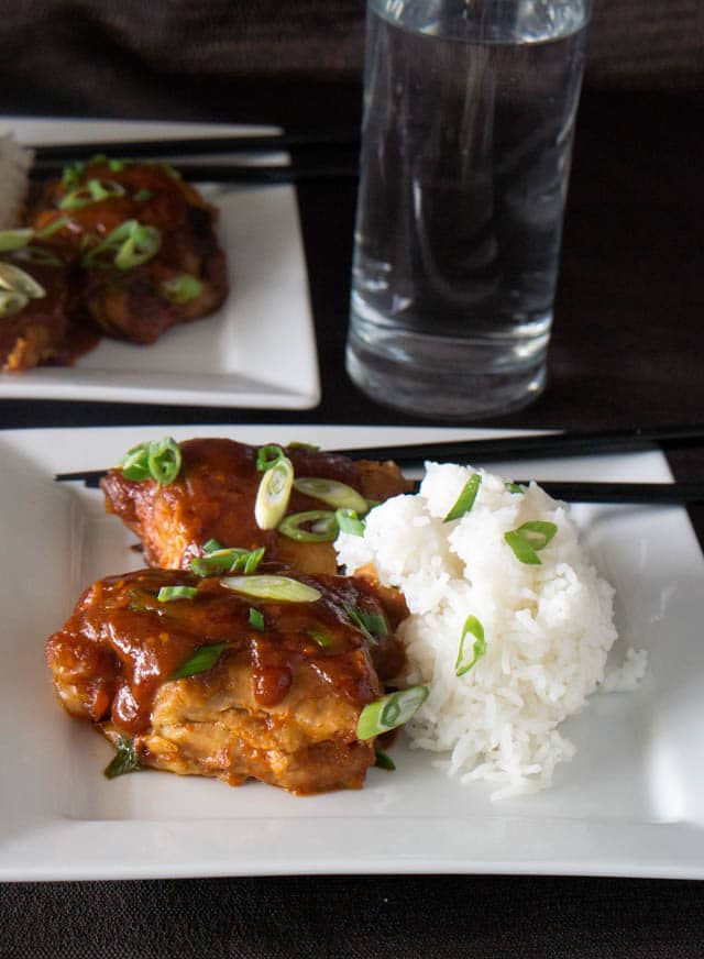 two white dinners plates with Korean-style chicken thighs and white rice, all made in an electric pressure cooker