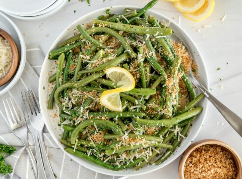 overhead shot of a white bowl of green beans with a lemon twist garnish and breadcrumbs