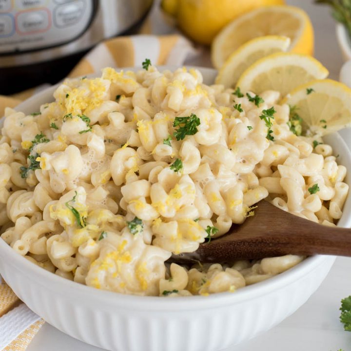 A shallow bowl filled with creamy lemon pasta, with lemon zest and parsley as garnishgarnished in the background, with additional lemon