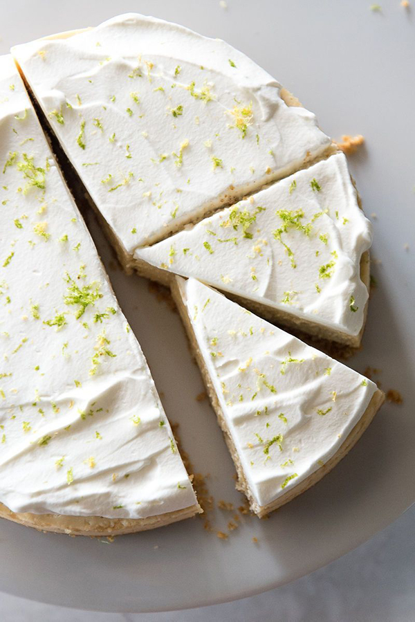 overhead shot of Instant Pot Key Lime Pie from Mountain Mama Cooks' review of Instantly Sweet - featuring a white plate with a creamy off-white cheeseake topped with white whipped cream and garnished with lime zest