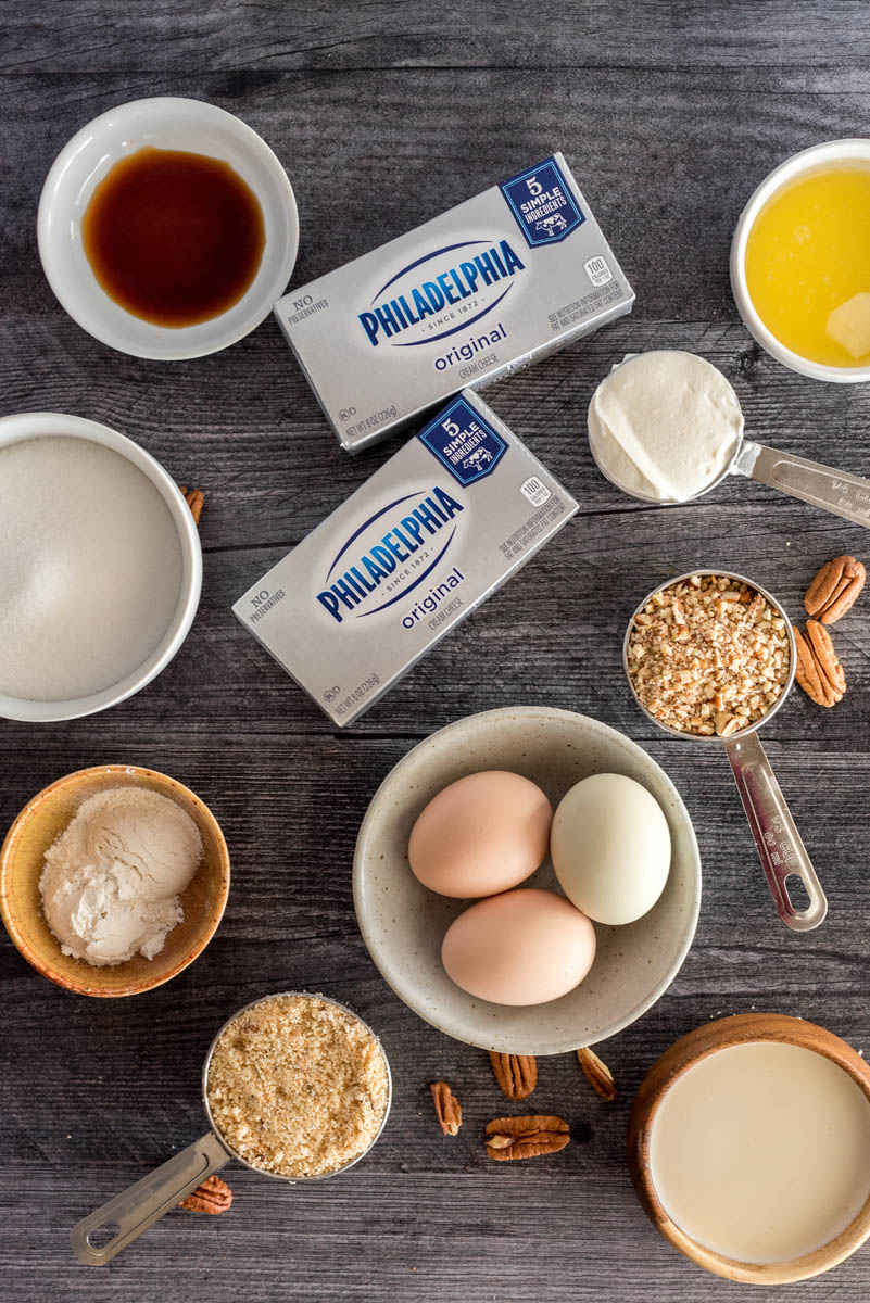 Overhead shot of ingredients for Instant Pot New York cheesecake, including cream cheese, sour cream, butter, vanilla, eggs, and crumbled shortbread cookies.