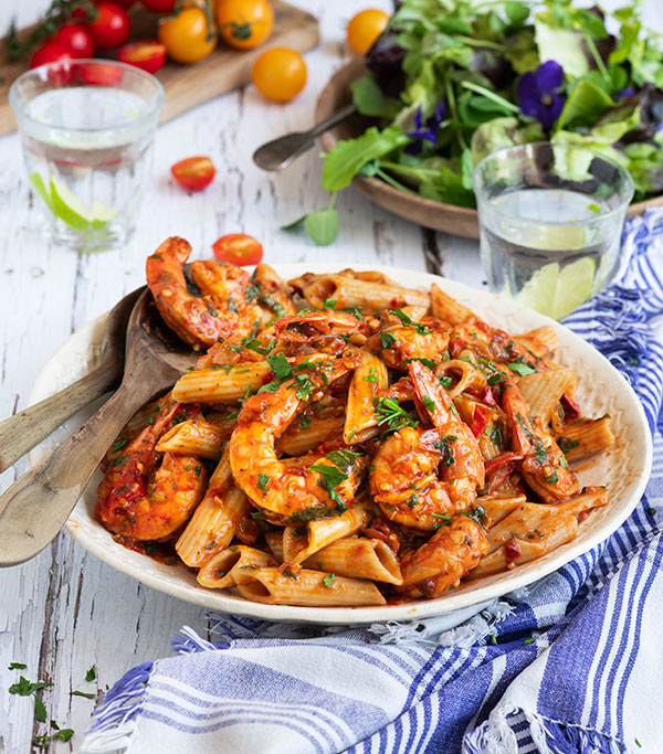 Instant Pot Shrimp Fra Diavlo over Penne Pasta in a white bowl with wooden serving spoons and a blue and white checkered cloth.