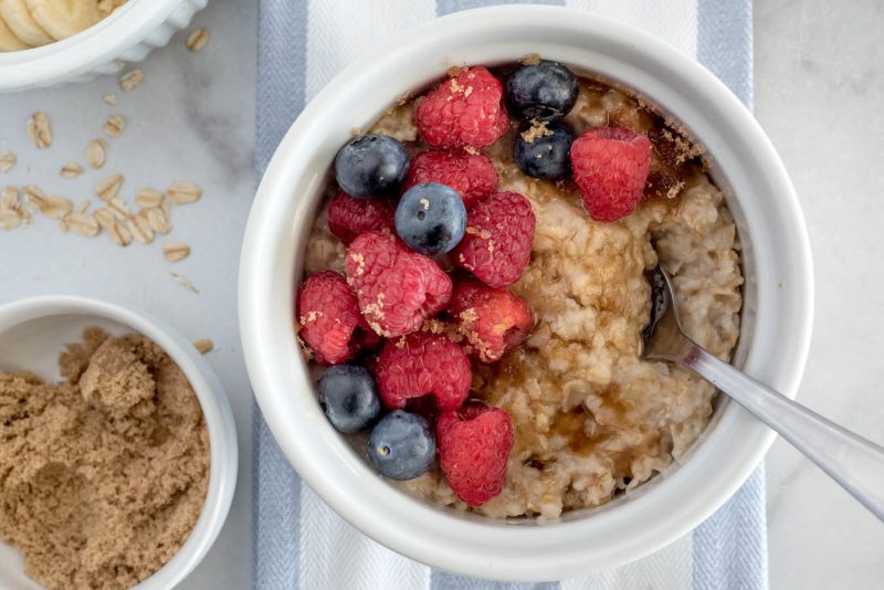 Close up shot of Instant Pot oatmeal for one topped with brown sugar, blueberries, and raspberries, with a bowl of brown sugar to the side.