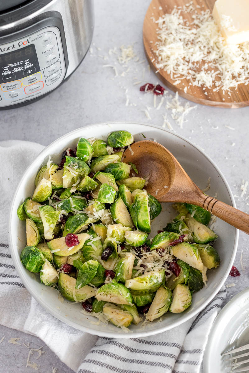 an overhead shot of a bowl of Brussels sprouts in front of an Instant Pot and a serving dish of shredded parmesan cheese