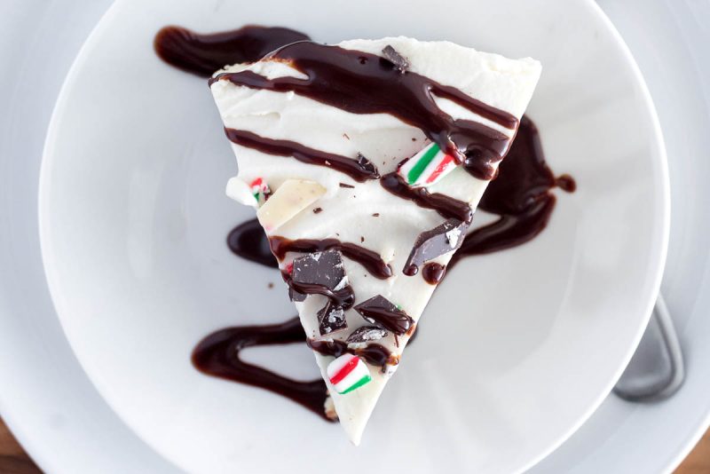 a close-up overhead shot of Christmas Peppermint Cheesecake, with a dark chocolate drizzle, candy canes, and white chocolate peppermint bark on top