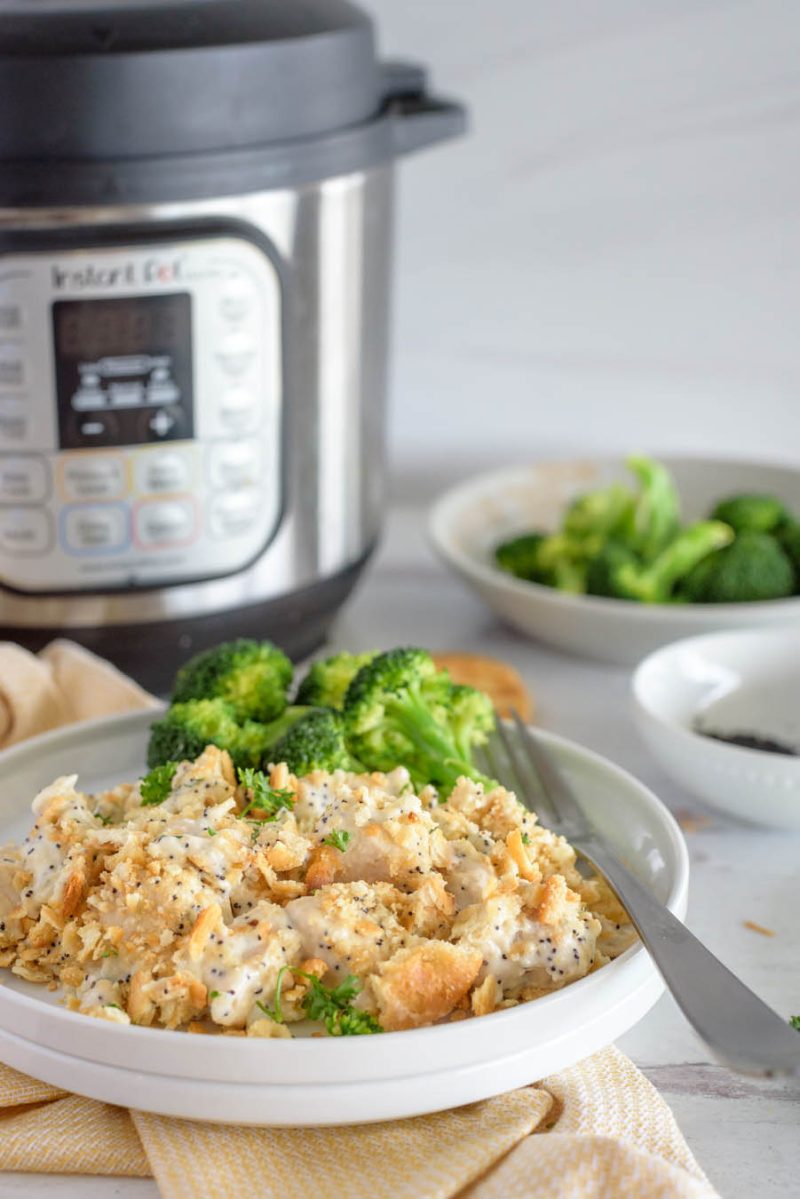 a 45 degree shot showing a white plate of poppy seed chicken casserole in front of an Instant pot with steamed broccoli in the background