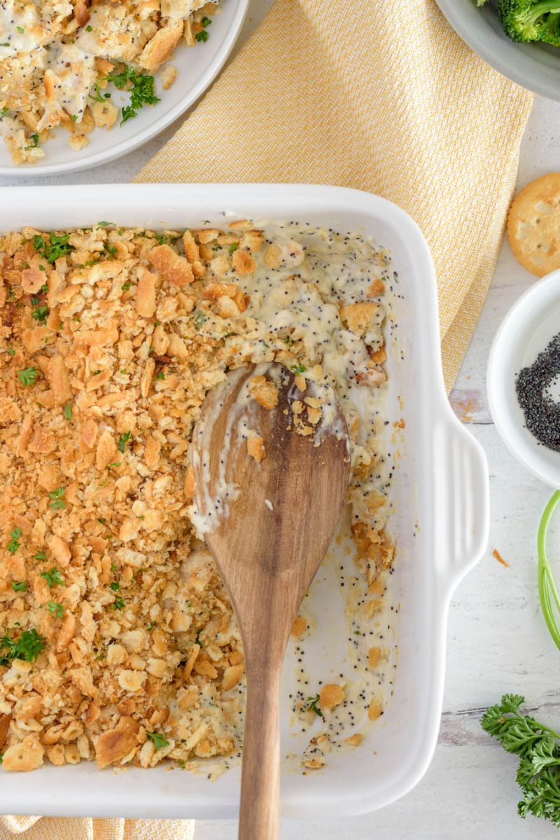 an overhead shot of a white rectangular casserole dish with a wooden spoon scooping out some of the poppy seed chicken casserole