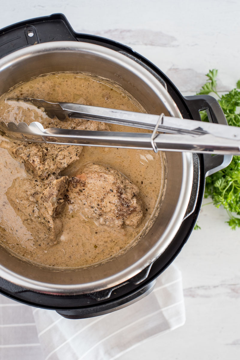 removing pork chops from an instant pot with metal tongs