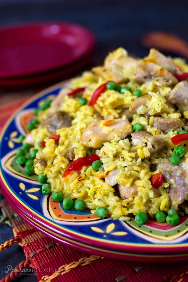 Arroz con Pollo is a saffron braised chicken and rice recipe for the pressure cooker. This delicious Mexican chicken dinner is served family style on a large platter garnished with pimiento and peas. colorful platter of Pressure Cooker Arroz con Pollo