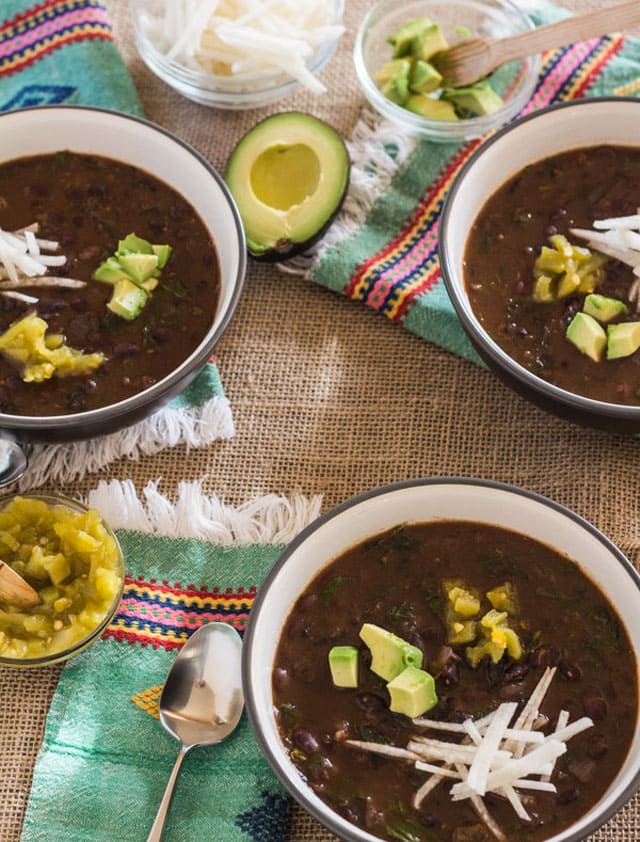 overhead photo of a table setting with 3 bowls of spicy black beans and hearty greens, made in an electric pressure cooker