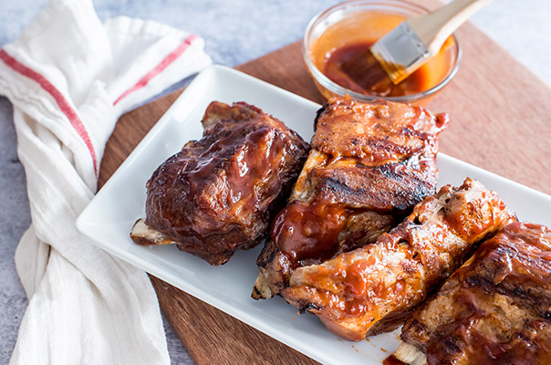 Baby Back Ribs on a white plate with BBQ sauce and a basting brush behind