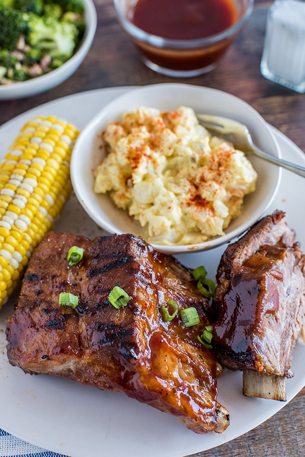A plate of Baby Back Ribs, corn on the cob, and potato salad ready to serve.