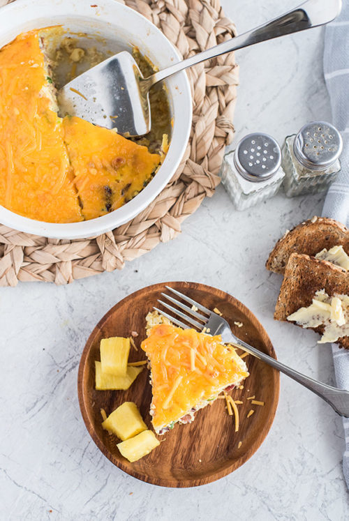 An above shot of a slice of Meat Lovers Quiche with pineapple on the plate and the cooking ramekin of quiche in the background