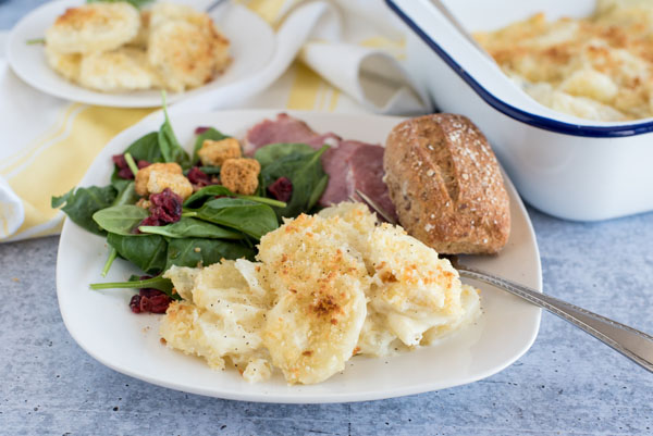 Instant Pot Potatos au Gratin made in a pressure cooker and plated with salad, ham, and a roll.