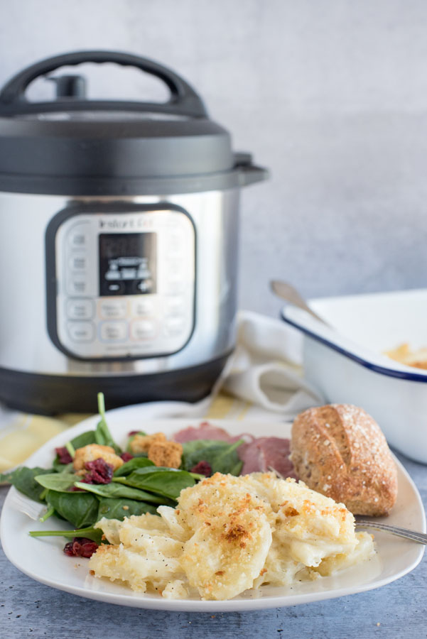 Cheesy Au Gratin Potatoes on a plate in front of an Instant Pot