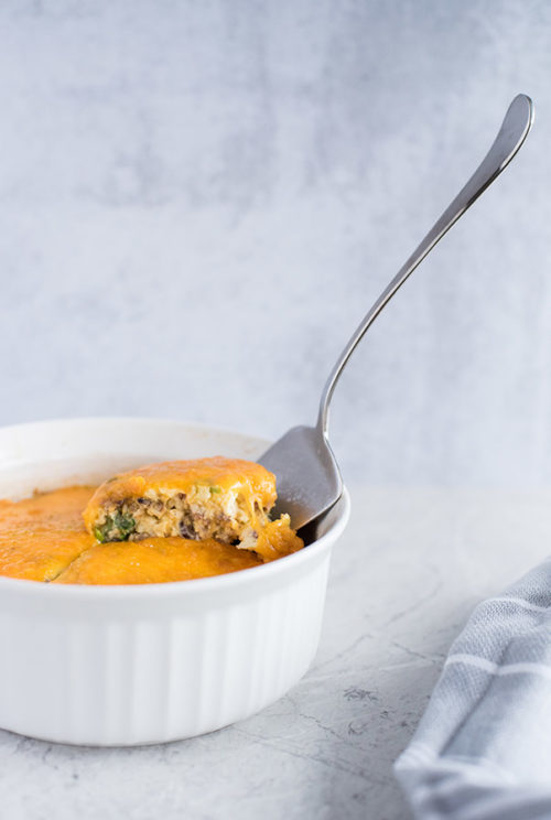 A silver serving utensil in the process of removing a slice of quiche from a white souffle dish