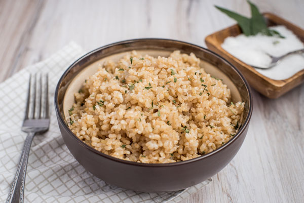 A dark brown bowl full of short-grain brown rice, prepared in teh Instant Pot, with a garnish of sea salt in the background