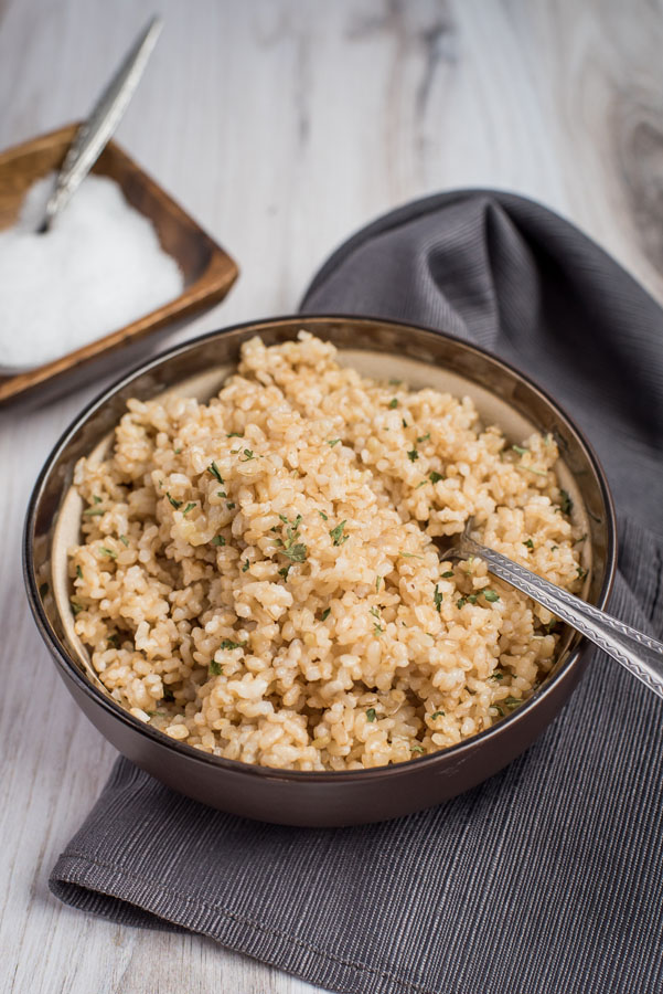 A small bowl of pressure cooker brown rice, with a small dish of salt and a gray cloth napkin in the background