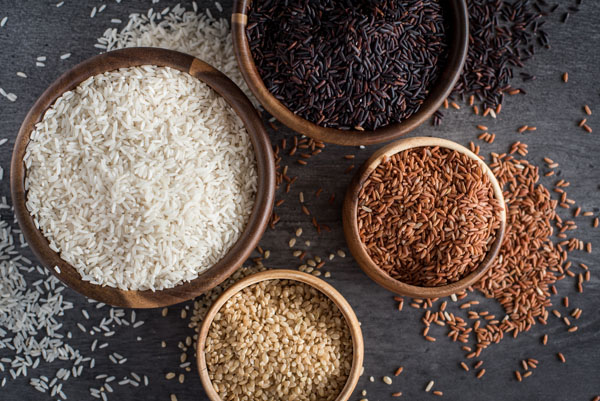 An overhead shot of four wooden bowls filled with different types of rice—white, brown, black, and pink