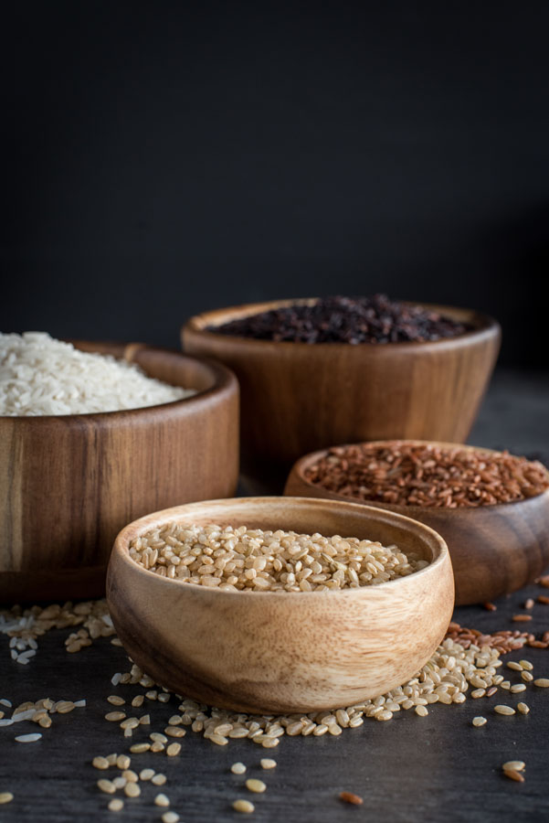 A side profile shot of four wooden bowls of different types of rice