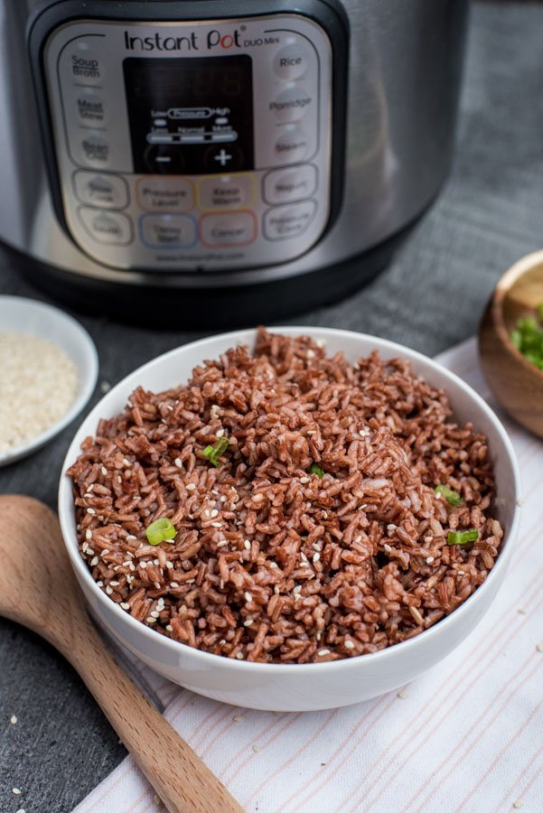 A white bowl filled with Pressure Cooker Pink Rice with an InstaPot, sesame seeds, and a wooden spoon in the background