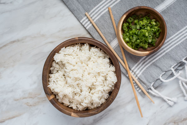An overhead shot of white rice prepared in the Instant Pot and green onions, with chopsticks balanced between the bowls