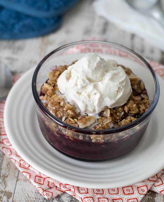45 degree shot included in the Instantly Sweet Dessert Cookbook - featuring a white plate and a small glass bowl of berry crisp with a melting scoop of vanilla ice cream on top