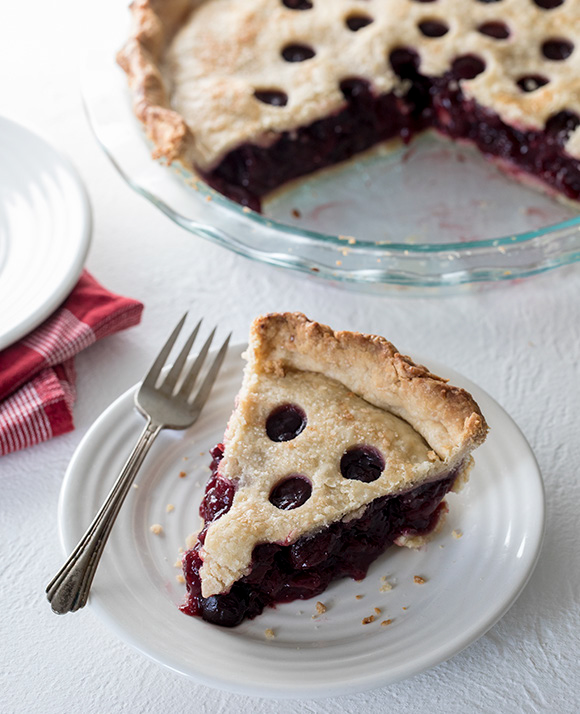 45 degree shot included in the Instantly Sweet Dessert Cookbook - featuring a slice of berry pie on a white plate, with a golden brown pie crust with three perfectly round holes on top