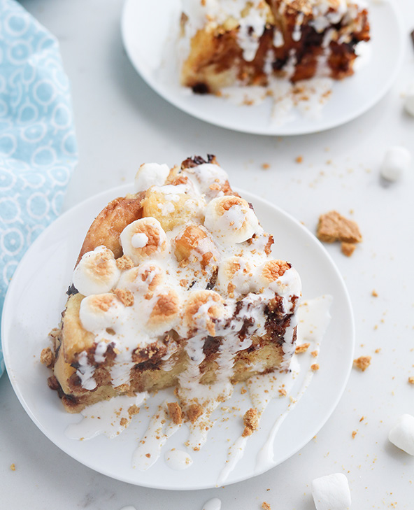 45 degree shot included in the Instantly Sweet Dessert Cookbook - featuring a white plate topped with a large slice of smores bread pudding, with broiled marshmallows, crushed graham crackekrs, and a marshmallow sauce drizzle on top